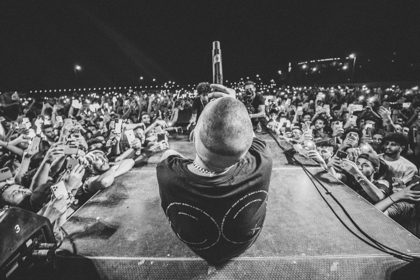 Artista visto de espaldas sobre el escenario, frente a un público entregado que graba con el móvil